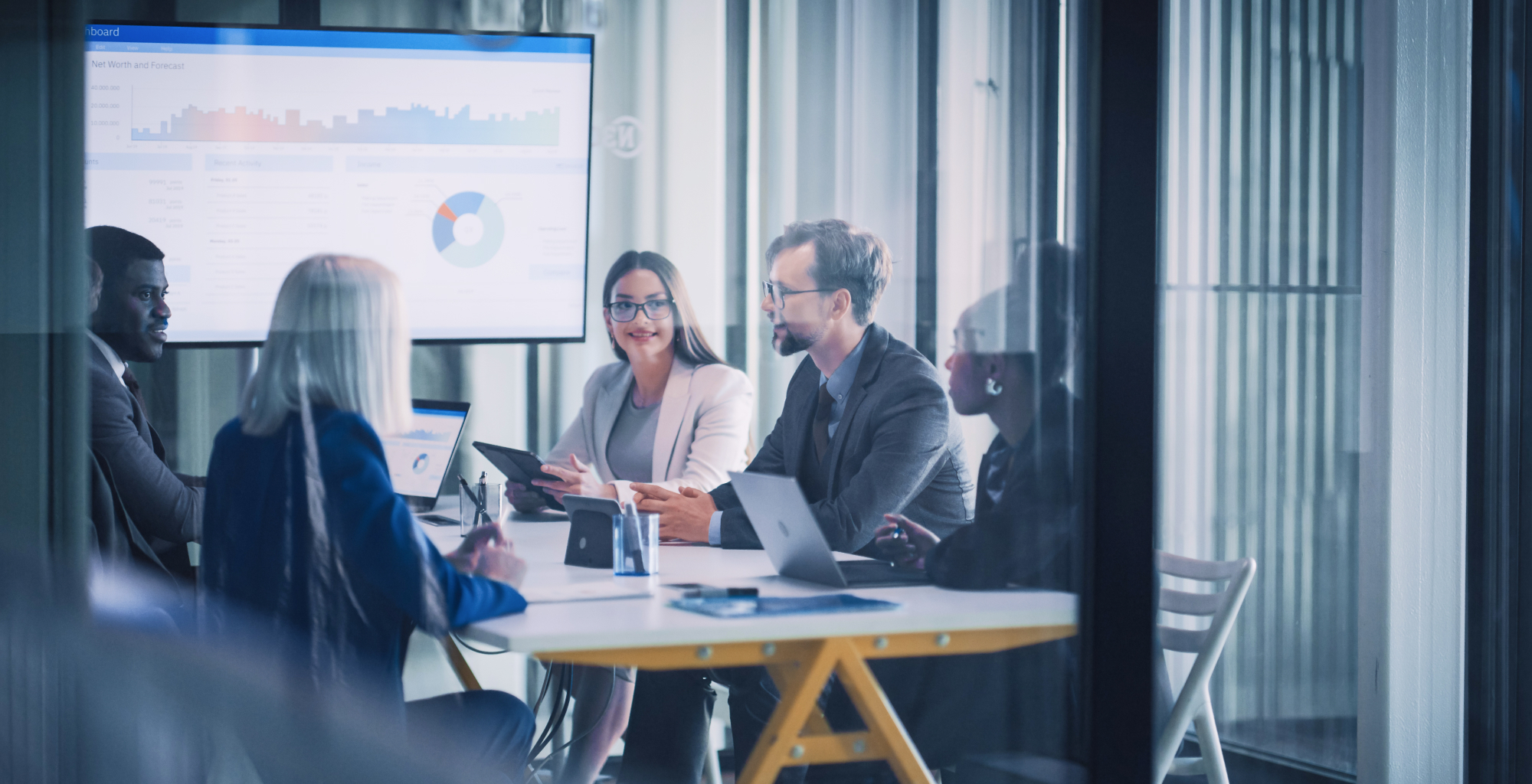 Equipo de profesionales reunido en una oficina con portátiles y una pantalla que muestra gráficos y datos empresariales, en Telefónica Tech.