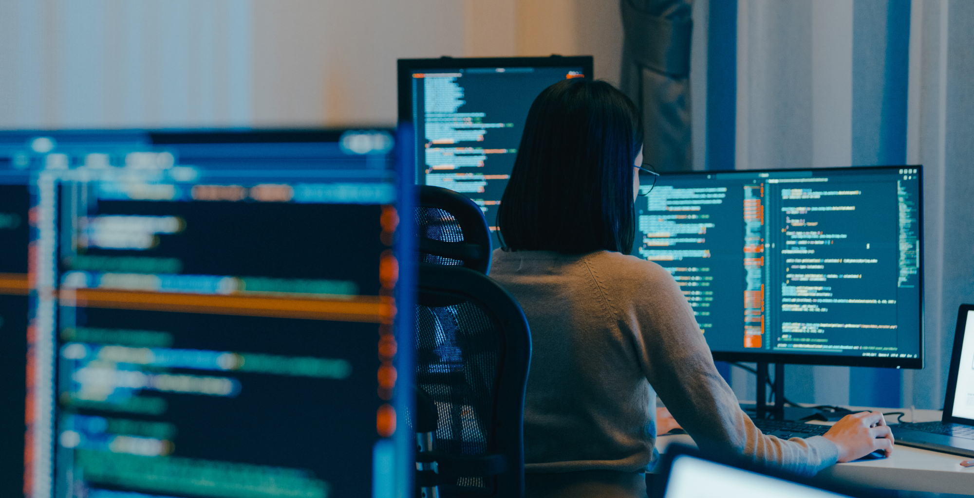 Profesional trabajando frente a varios monitores que muestran líneas de código y herramientas de programación en un entorno tecnológico de Telefónica Tech.